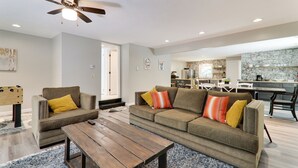 A living room with a sofa, two armchairs, a coffee table, and a ceiling fan. There is a kitchen in the background with a stone backsplash and modern appliances. - Large home & 5 min to Kalahari, Gather here at WOODLAND RETREAT! (Pocono Summit)