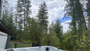 Un jacuzzi rodeado por una zona boscosa con árboles altos y un cielo despejado.