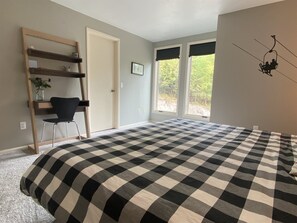 Ein Schlafzimmer mit einem großen Bett, einem Sessel, einem Schreibtisch und einem Fenster mit Blick auf Bäume.