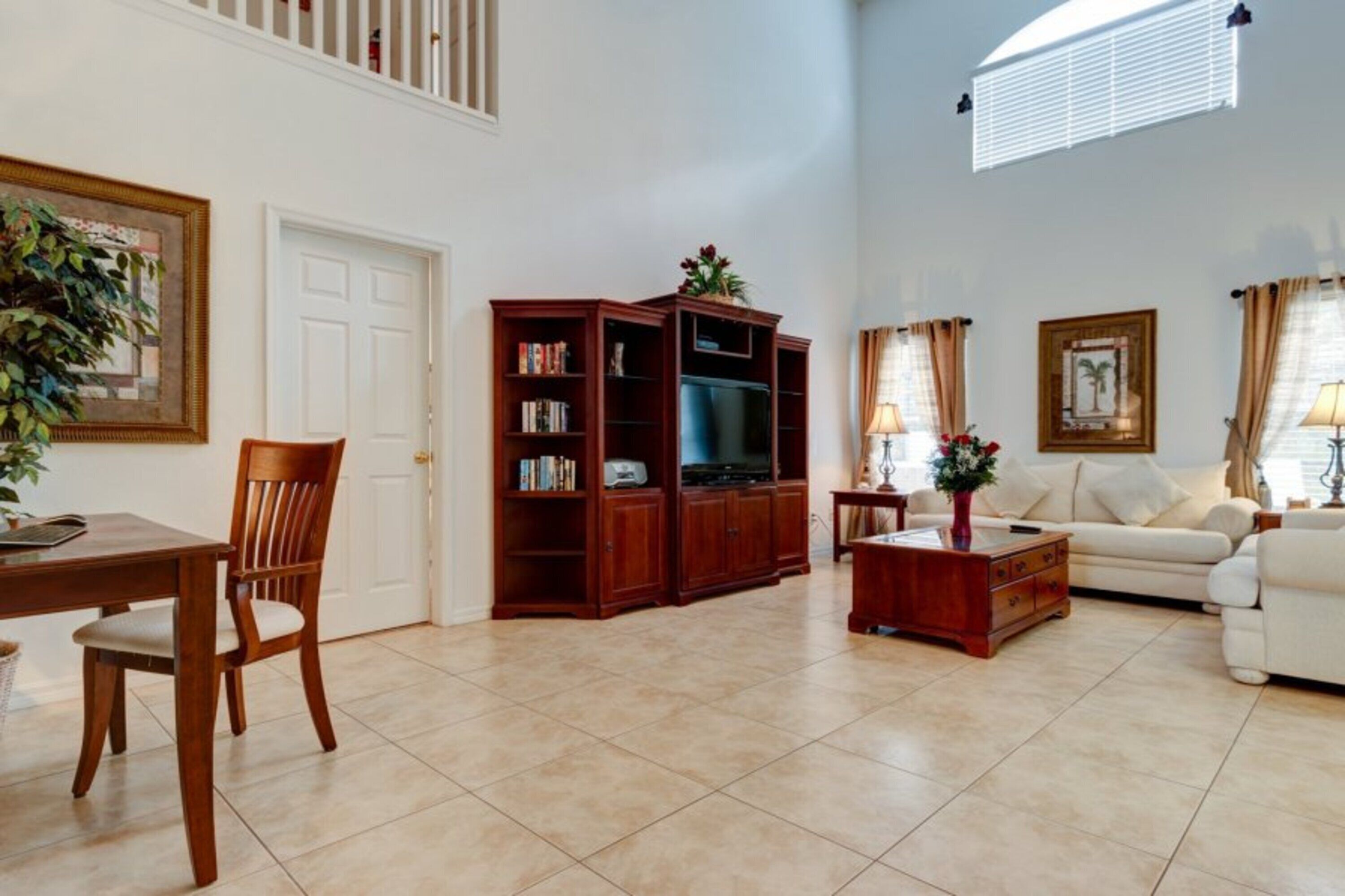 A living room with a wooden entertainment center, a white sofa, a dining table with a chair, and a potted plant.