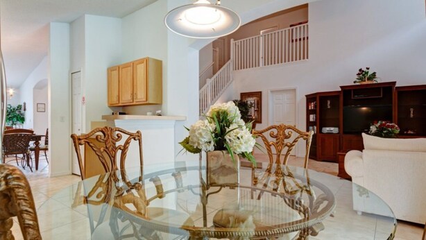 A spacious living room with a glass-top dining table surrounded by ornate chairs, a white sofa, and a staircase leading to an upper level. - SKC Villa Emerald Island Resort (Kissimmee)