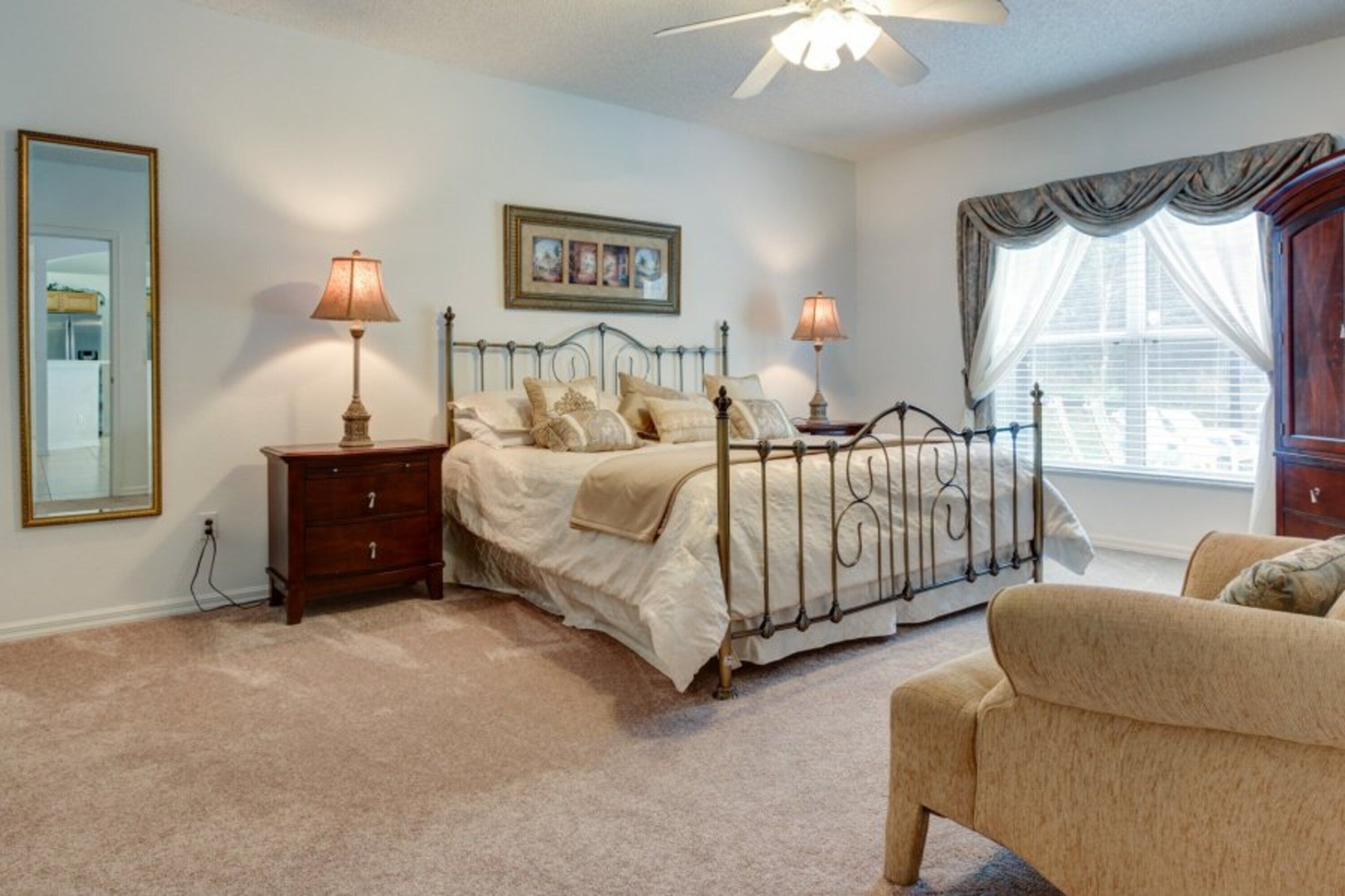 A bedroom with a bed, bedside lamps, a dresser, a chair, a window with curtains, and a ceiling fan.