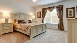 A bedroom with a bed, two bedside tables, a ceiling fan, a window with curtains, and a framed picture on the wall. - SKC Villa Emerald Island Resort (Kissimmee)