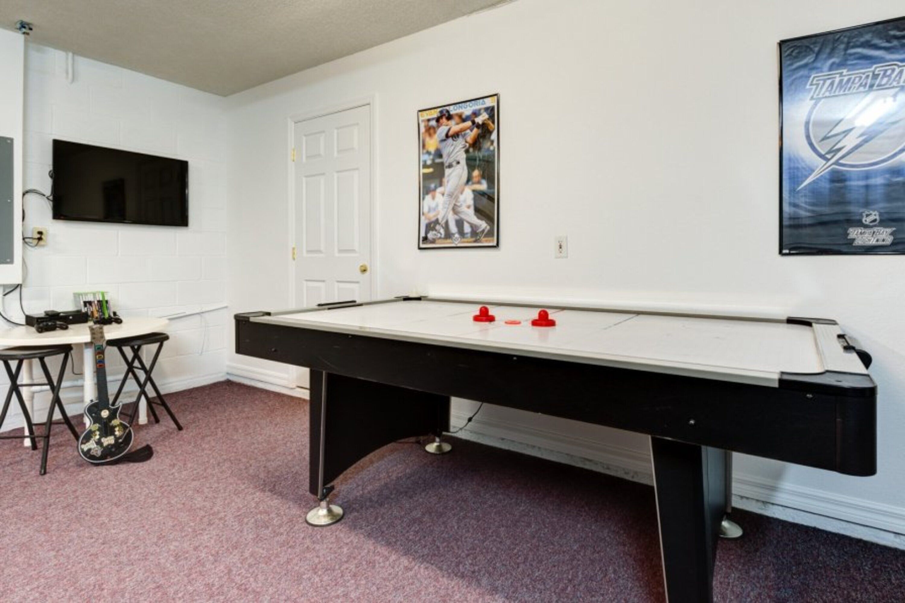 Ein Billardtisch in einem Raum mit weißen Wänden, einem an der Wand befestigten Fernseher und einem Plakat eines Baseballspielers.