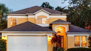 A two-story house with a white garage door, a small porch with a railing, and a well-maintained lawn. - SKC Villa Emerald Island Resort (Kissimmee)
