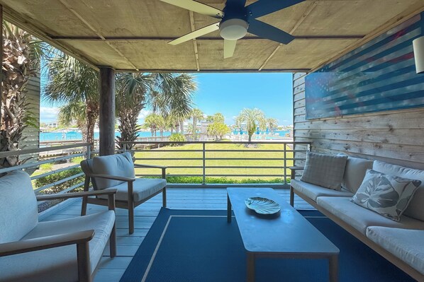 A covered outdoor seating area with a ceiling fan, a view of the pool, and a wooden wall with a flag.