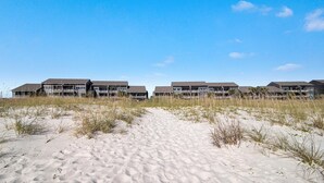 Ein Strandhotel mit mehreren Gebäuden, einem Sandweg zum Eingang und einem wolkenlosen, blauen Himmel.