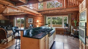 A log cabin interior with a kitchen island, bar stools, and a dining area.