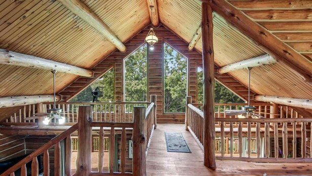 An attic-style room with wooden beams, a central window, and a wooden deck.