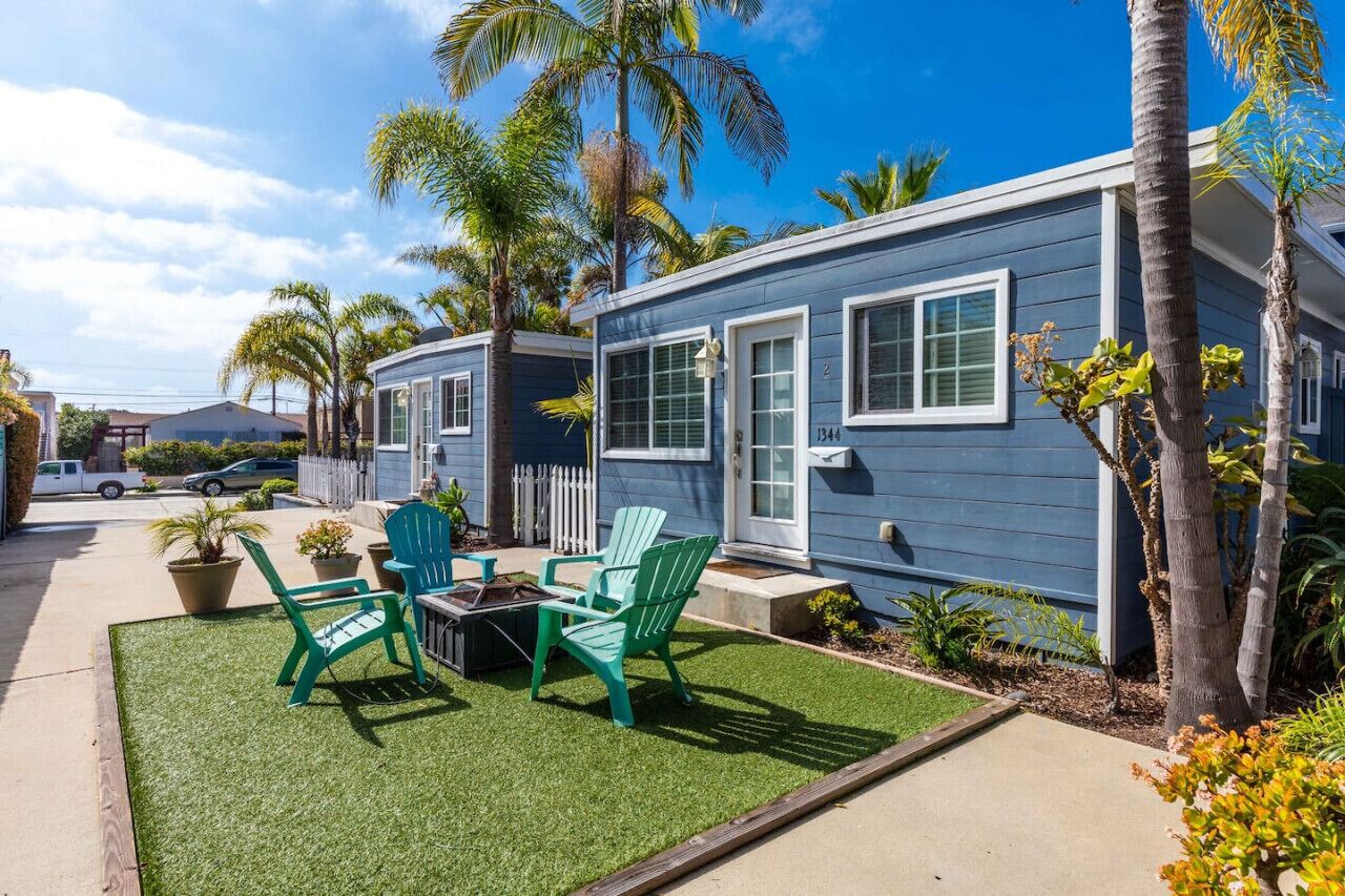 A two-story blue house with a small patio area featuring green chairs and a table.