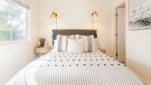 Ein Schlafzimmer mit einem großen Bett, zwei Nachttischlampen, einem kleinen Beistelltisch mit einer Pflanze und einem gerahmten Bild an der Wand.