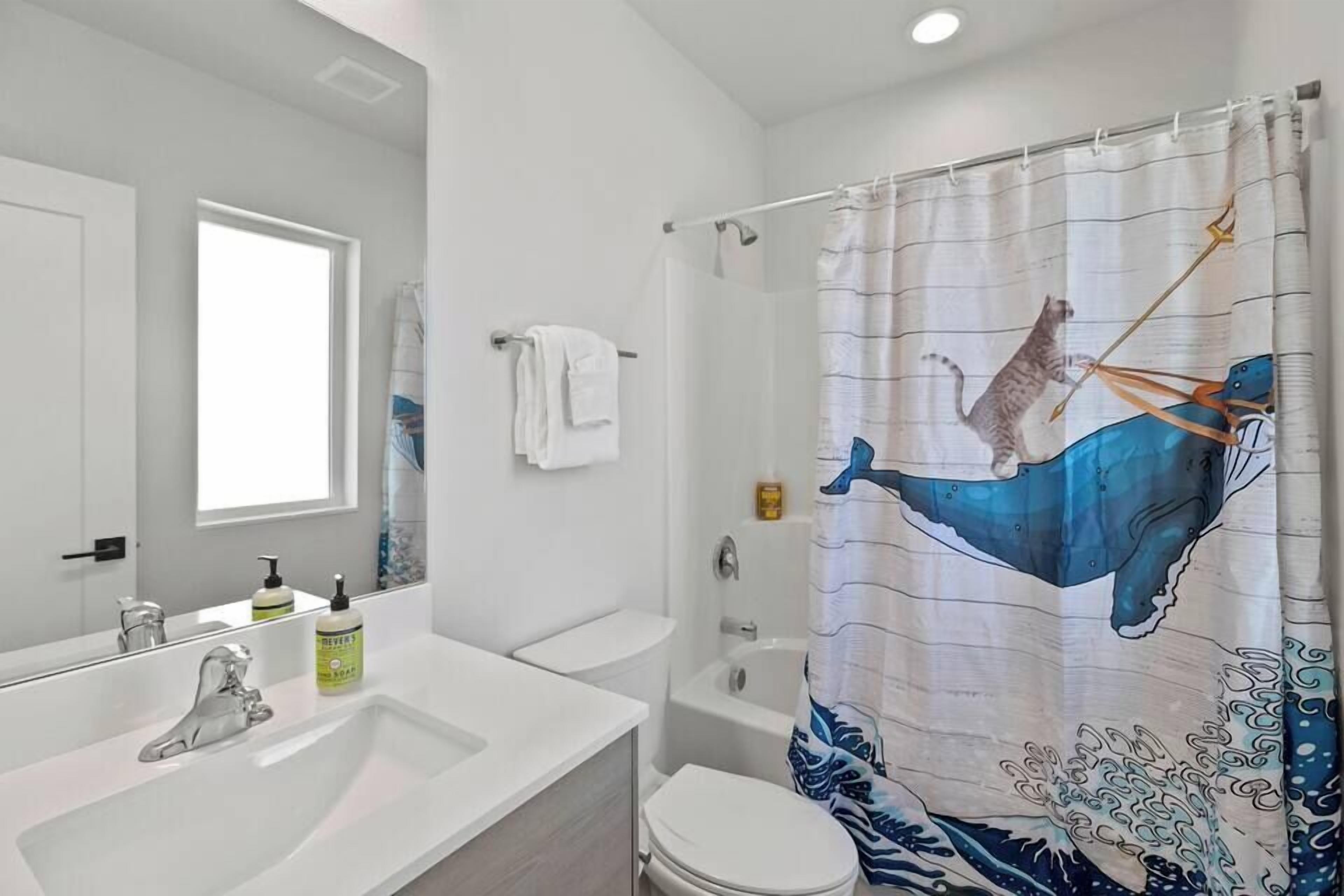 Een badkamer met een wit wastafel, spiegel en toilet. Er is een douchegordijn met een walvisprint.