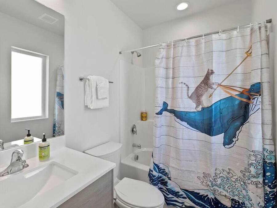 A bathroom with a white sink, mirror, and toilet. There is a shower curtain with a whale design.