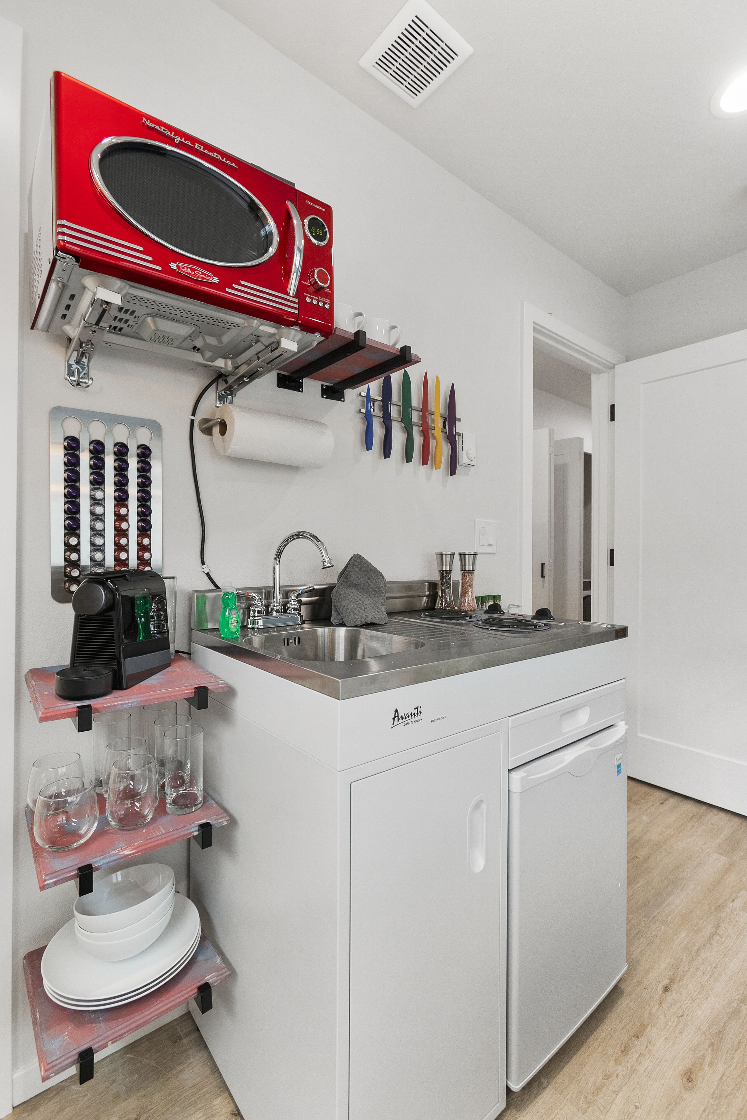 Een kleine keuken met een rode magnetron, een inbouwspoelbak en een compacte koelkast.