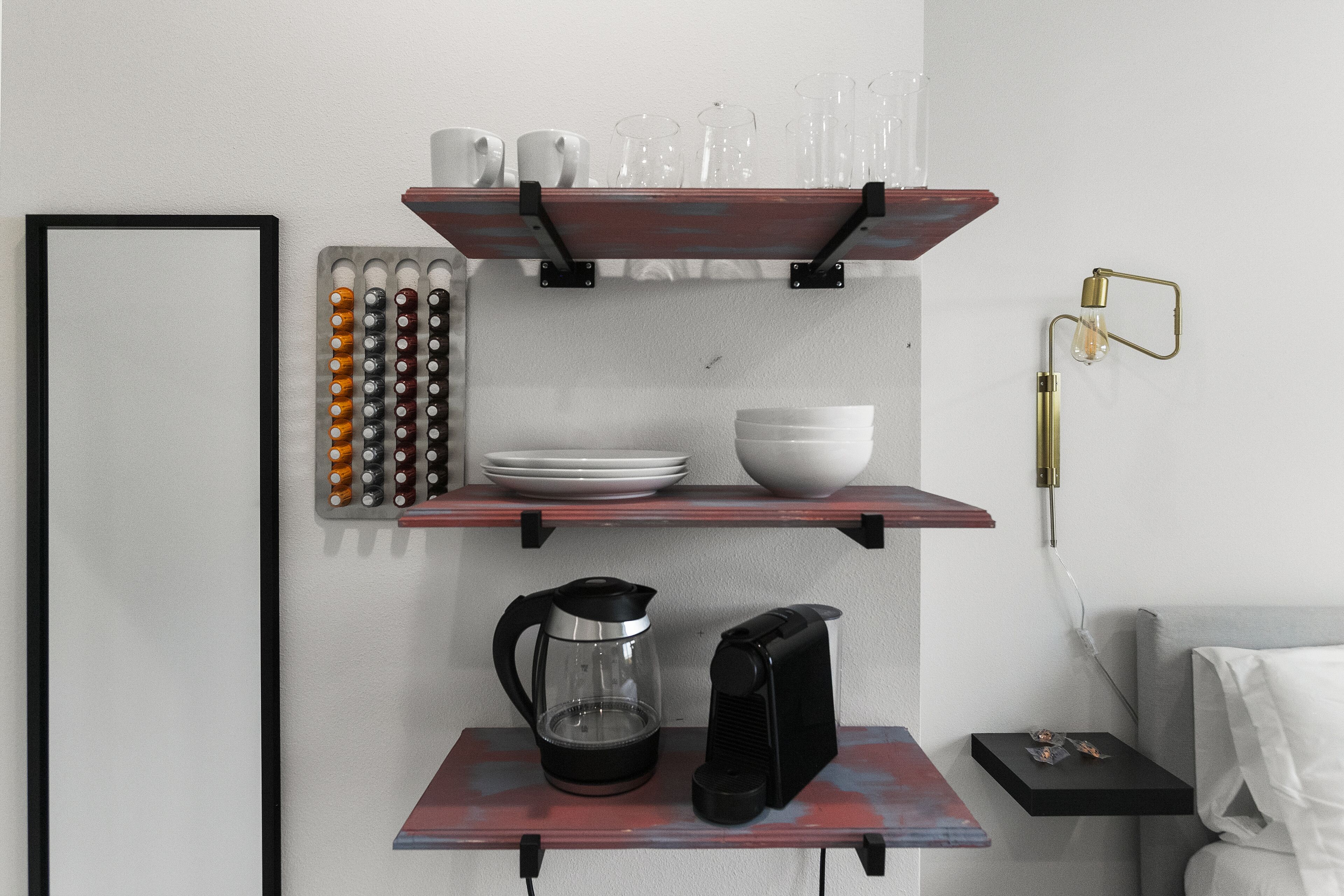 Et køkken med kaffemaskine, elkedel og hylder med tallerkener og glas.