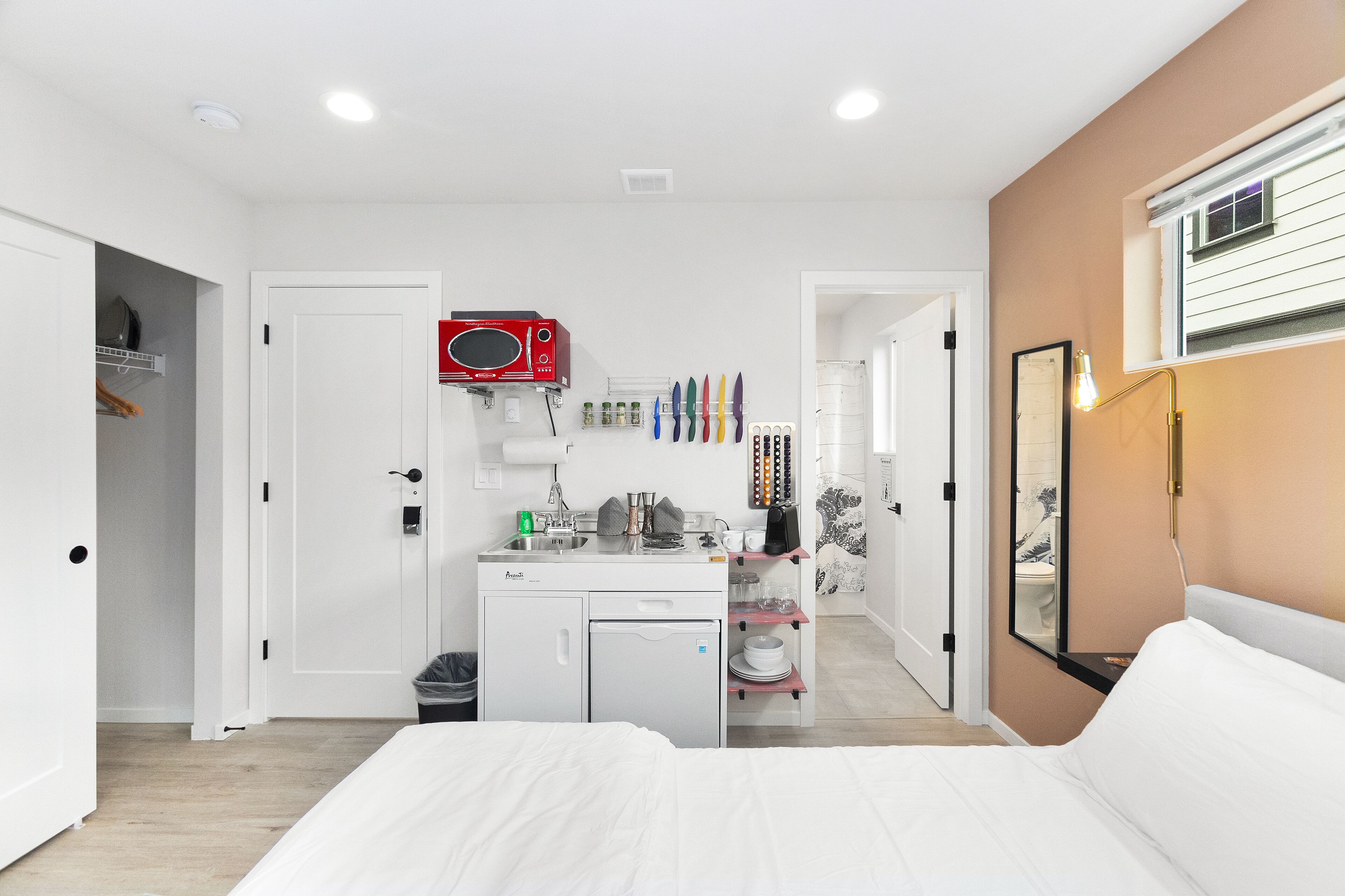 A compact hotel room with a kitchenette, a bed, a small fridge, and a bathroom.
