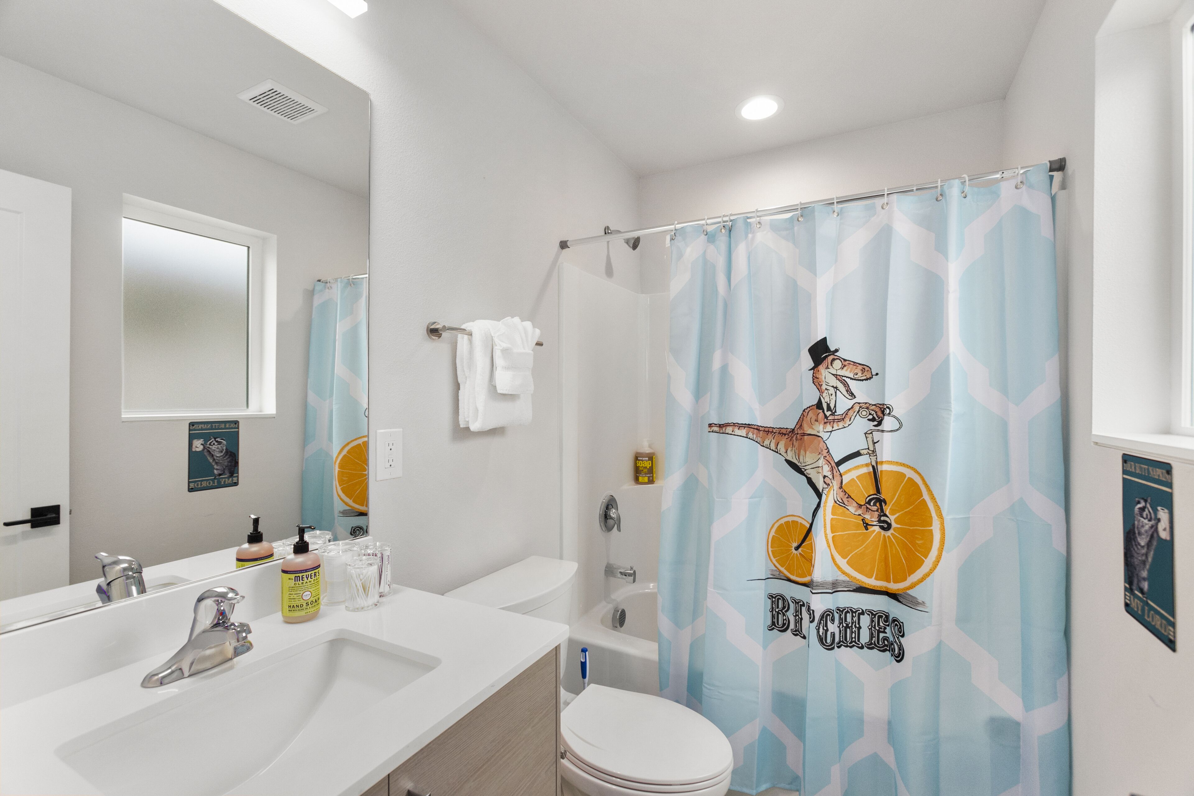 A bathroom with a white sink, mirror, and toilet. There is a shower curtain with a giraffe and orange design.