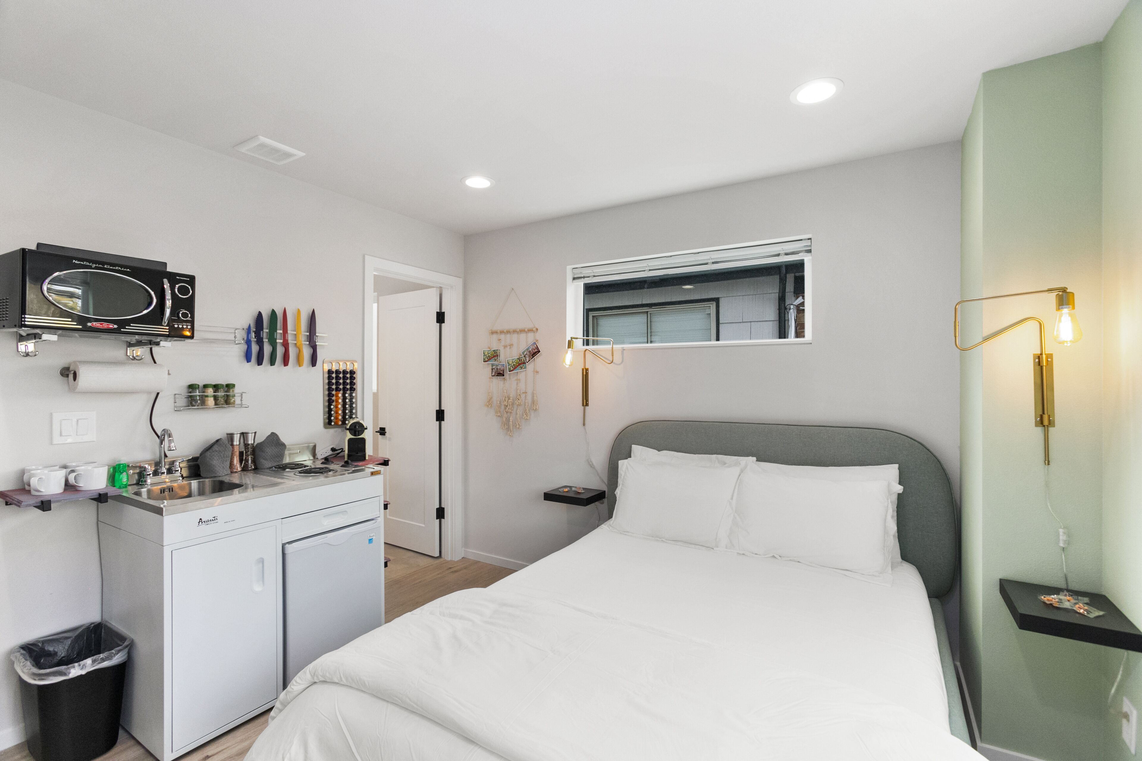 A modern hotel room with a bed, a small kitchenette, a microwave, and a window.