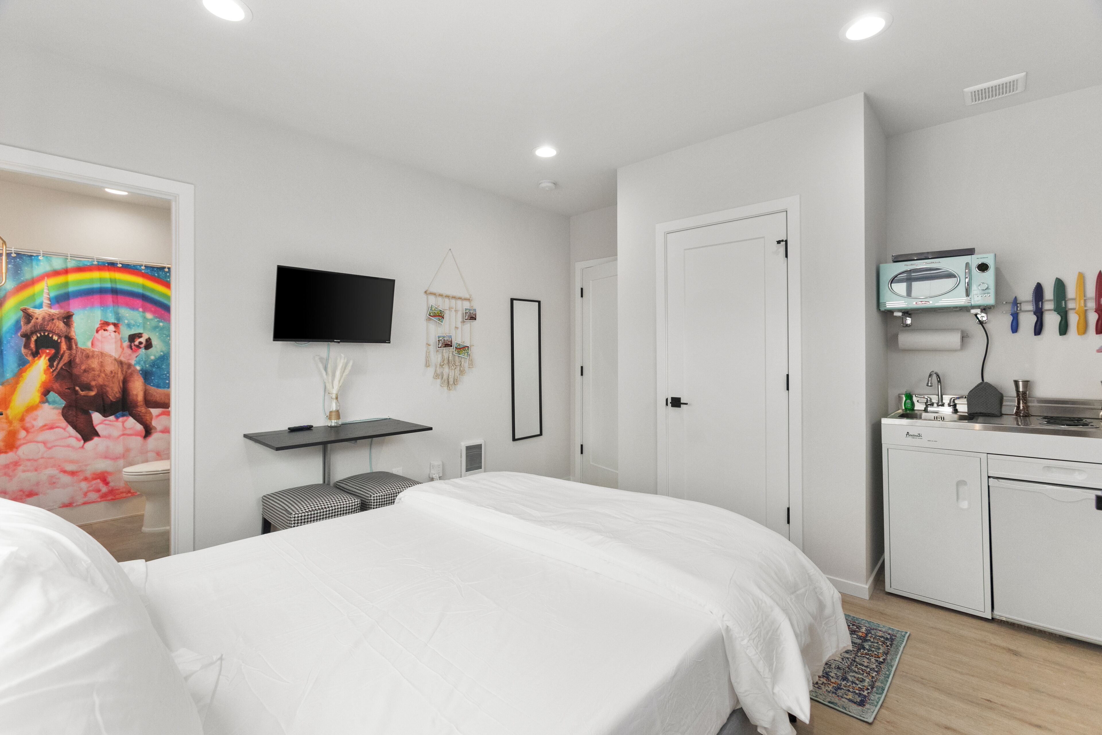 A modern bedroom with a bed, a TV, a small table, and a kitchenette.