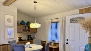 A dining area with a round table, four chairs, a hanging light fixture, and a kitchen in the background. - Convenient NE Albuquerque location, right off I-25!! (Albuquerque)