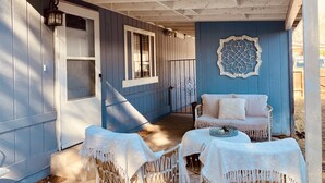 A covered porch with a blue exterior, two wicker chairs with white cushions, and a decorative wall piece. - Convenient NE Albuquerque location, right off I-25!! (Albuquerque)