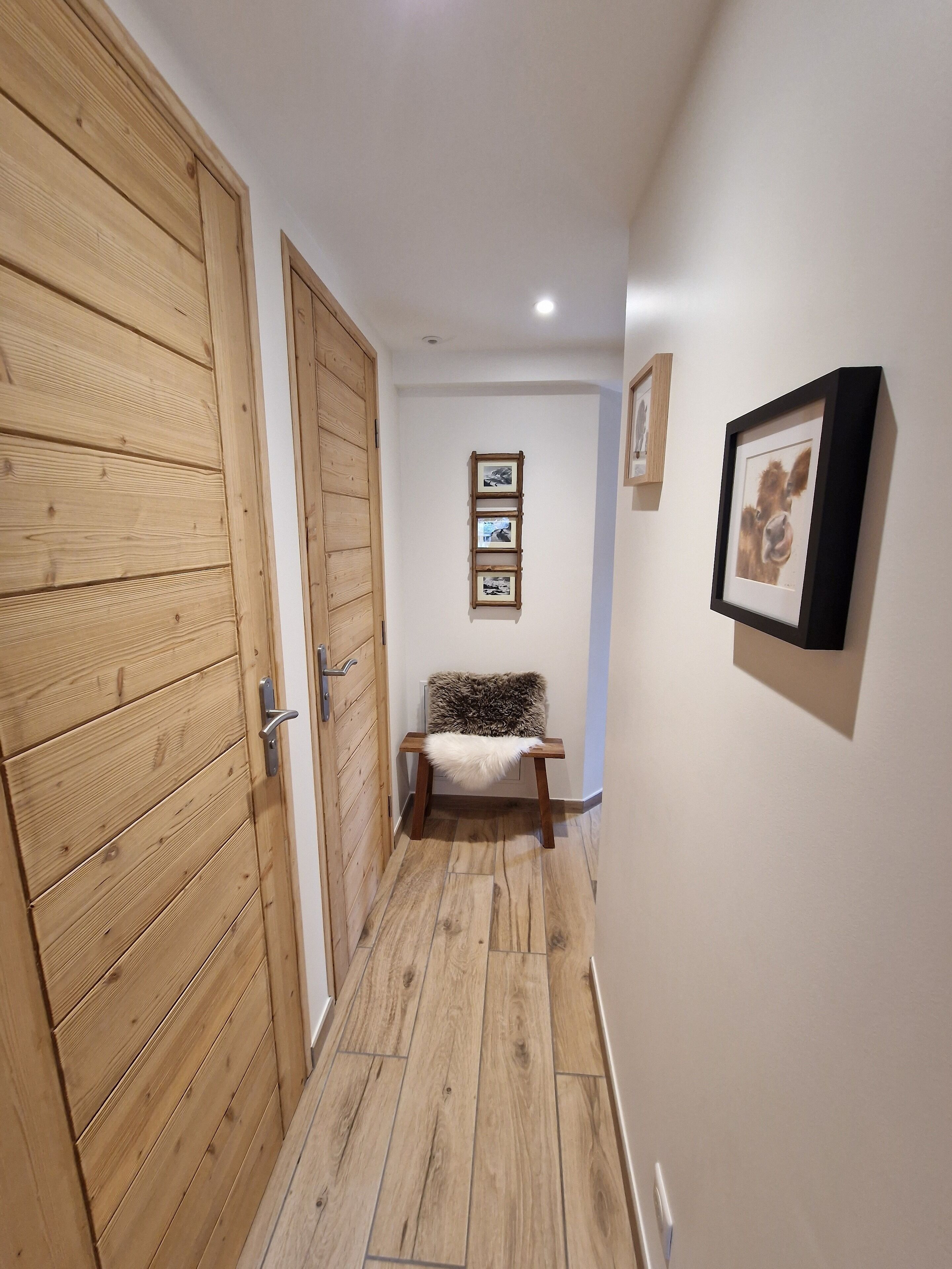 Un couloir doté d’un plancher en bois, d’un banc recouvert d’un plaid en fourrure et de tableaux encadrés accrochés au mur.