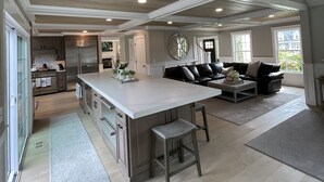 Een ruime woonkamer met een groot eiland, een keuken met moderne apparatuur en een gezellige zithoek met een bank en poef.