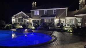 Een goed verlicht woonhuis met een zwembad, een terras en een groot herenhuis met meerdere ramen en een schoorsteen.