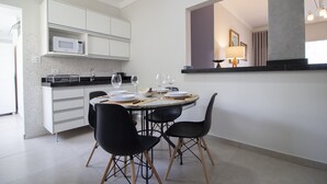 Une cuisine moderne avec des meubles blancs, un four à micro-ondes et un coin repas comprenant des chaises noires et une table dressée pour quatre personnes.