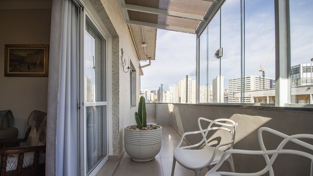 Un balcon agrémenté d’un cactus en pot, de chaises blanches et offrant une vue sur les immeubles de la ville.