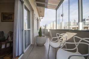 A balcony with a potted cactus, white chairs, and a view of city buildings. - Terraço na Liberdade Garagem Wifi 250 mb (São Paulo)