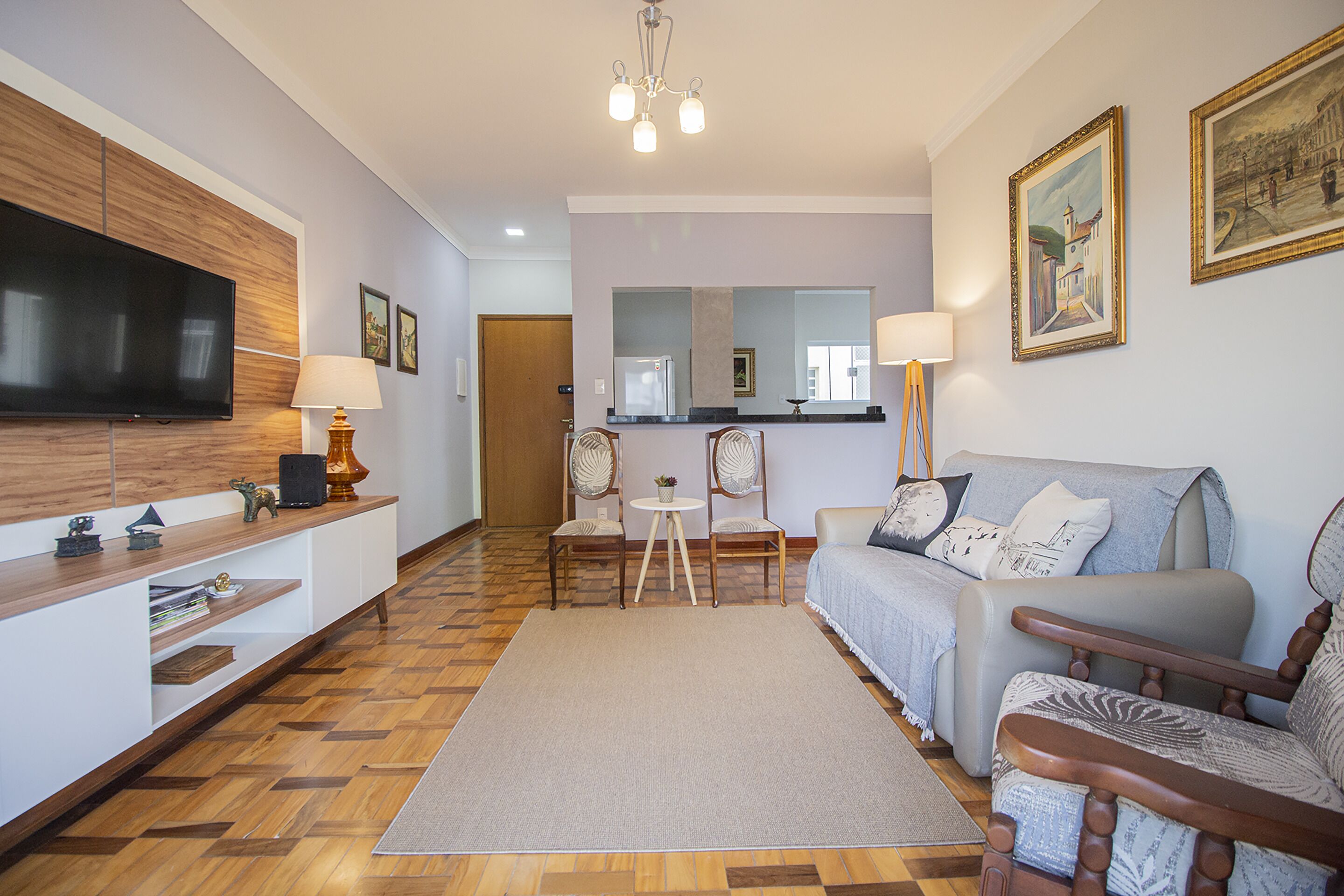 A modern living room with a flat-screen TV, wooden entertainment unit, sofa, chairs, and a dining area with a table and chairs.
