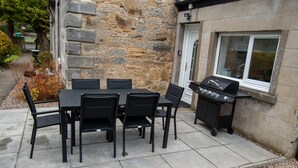 An outdoor patio with a stone wall, a grill, and a table with chairs. - Beautiful 200 year old Cottage near St Andrews (Markinch)