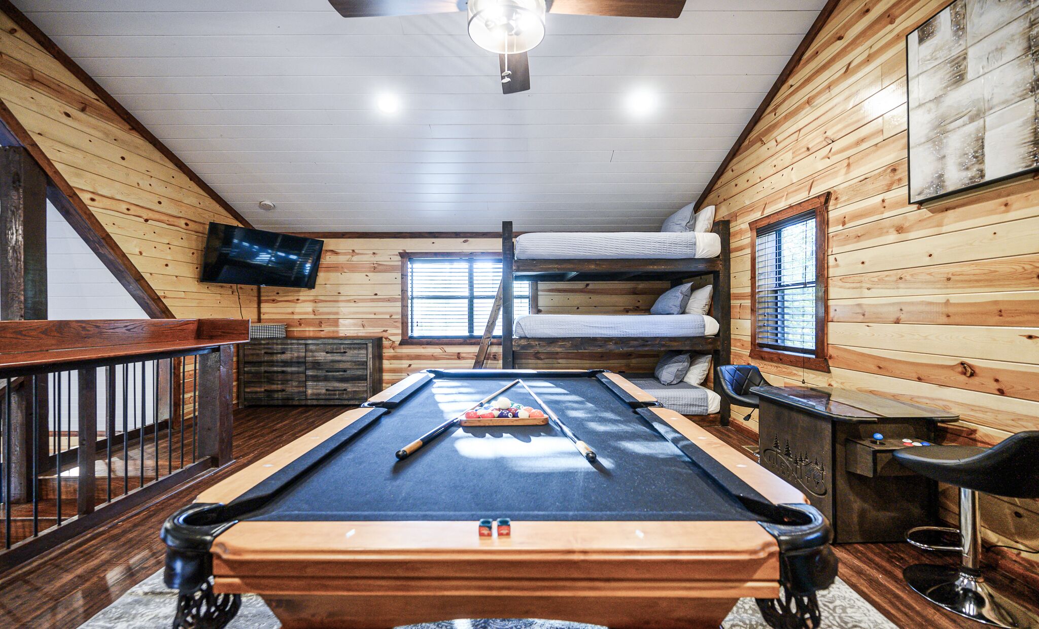 A pool table in a room with wooden walls, a bunk bed, a TV, and a window.
