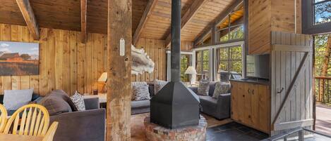 A rustic cabin interior with a fireplace, wooden walls, and a dining area.