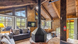 A cozy interior with a fireplace, wooden walls, and large windows. - Brecken Haus (Breckenridge)