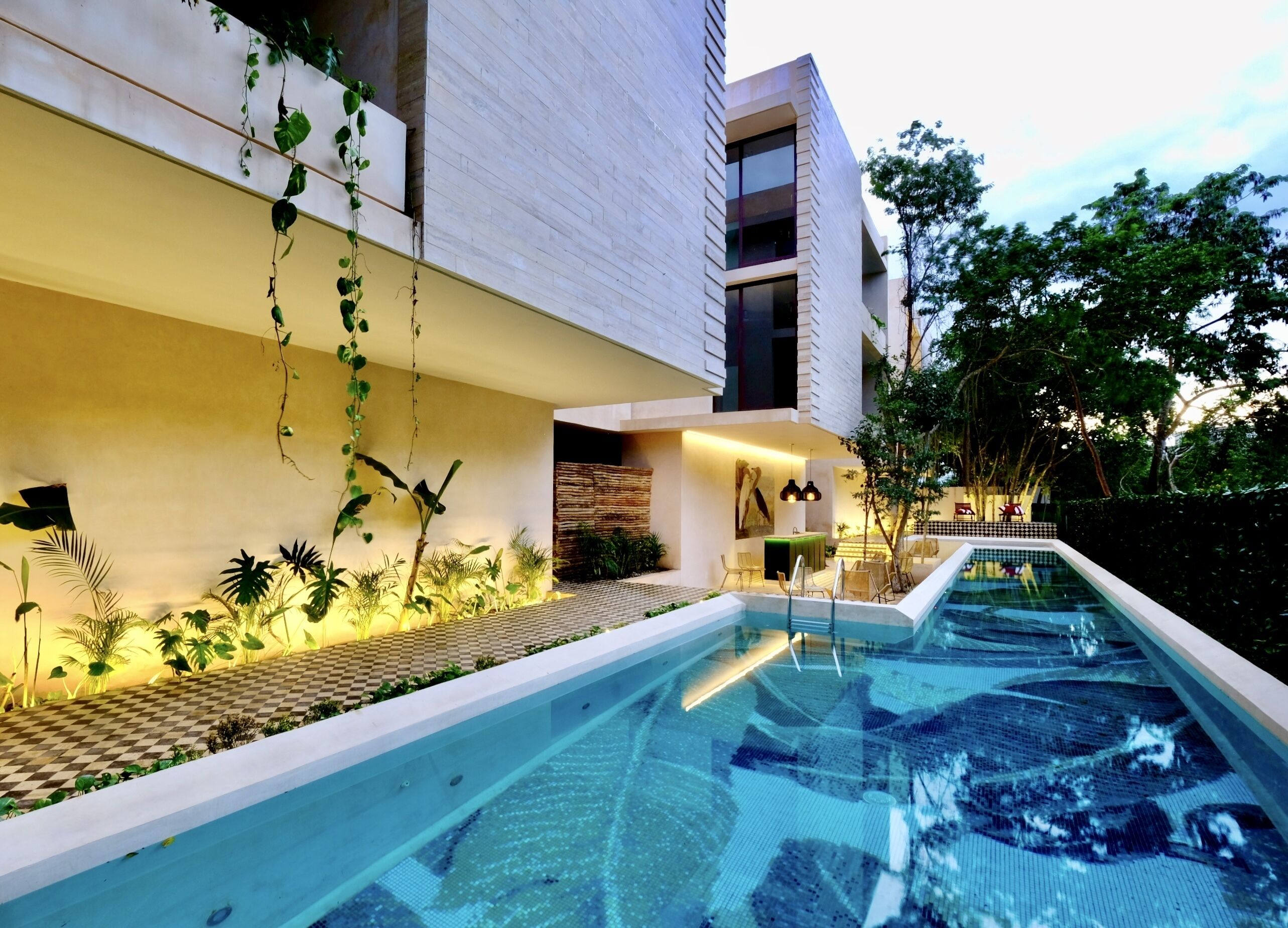 A modern building with a swimming pool, outdoor seating, and lush greenery.