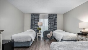 A hotel room with two beds, a small table with a lamp, a chair, and a desk with a lamp. - First Floor Standard Deluxe King (North East)