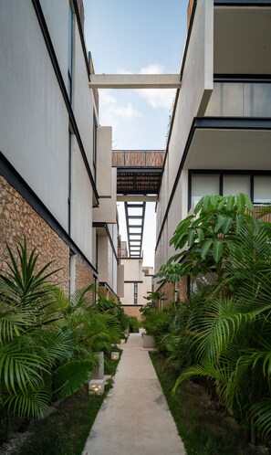 A modern building with a central courtyard, surrounded by lush greenery and a concrete pathway. - Two Bedroom Luxury Apartment by TuLuna (Tulum)