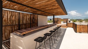 An outdoor bar area with a wooden ceiling, a long counter, and multiple bar stools. - Two Bedroom Luxury Apartment by TuLuna (Tulum)