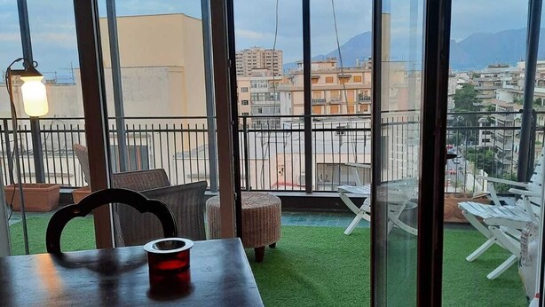 Una habitación con un gran ventanal corredera que da a un balcón con vistas a la ciudad y a las montañas.