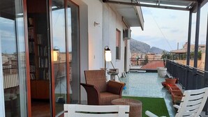 Un espacio exterior techado con piscina, sillas reclinables blancas, una mesa y una estantería.