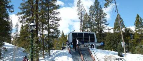 A ski lift station with a chairlift, surrounded by snow-covered slopes and tall evergreen trees.