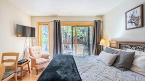 Hotellihuone, jossa on sänky, televisio, tuoli, työpöytä ja liukuoven kautta avautuva näkymä ulos.