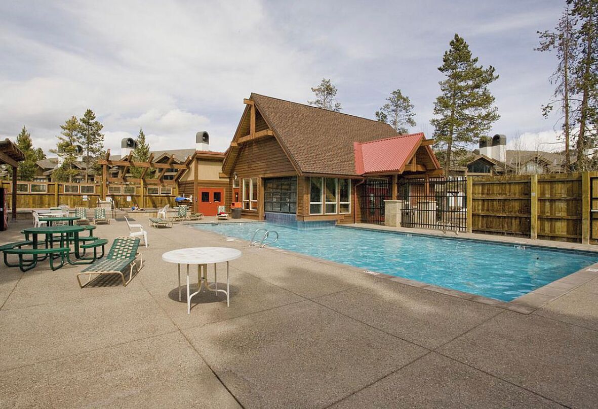 Un espace piscine agrémenté d’un bâtiment en bois, de tables de pique-nique et de chaises longues.