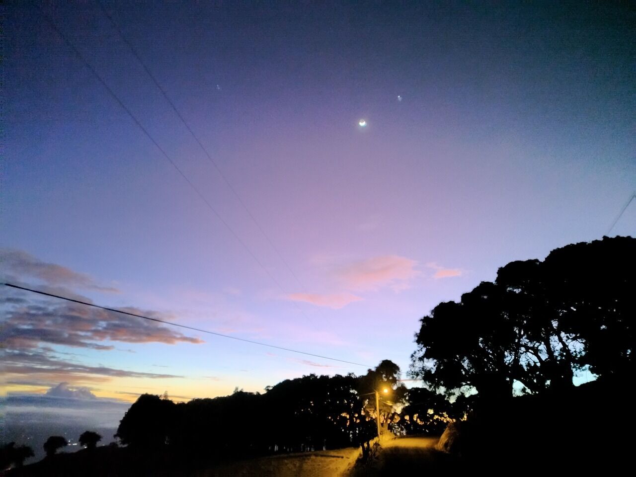 A twilight sky with a visible moon and streetlights illuminating a road.