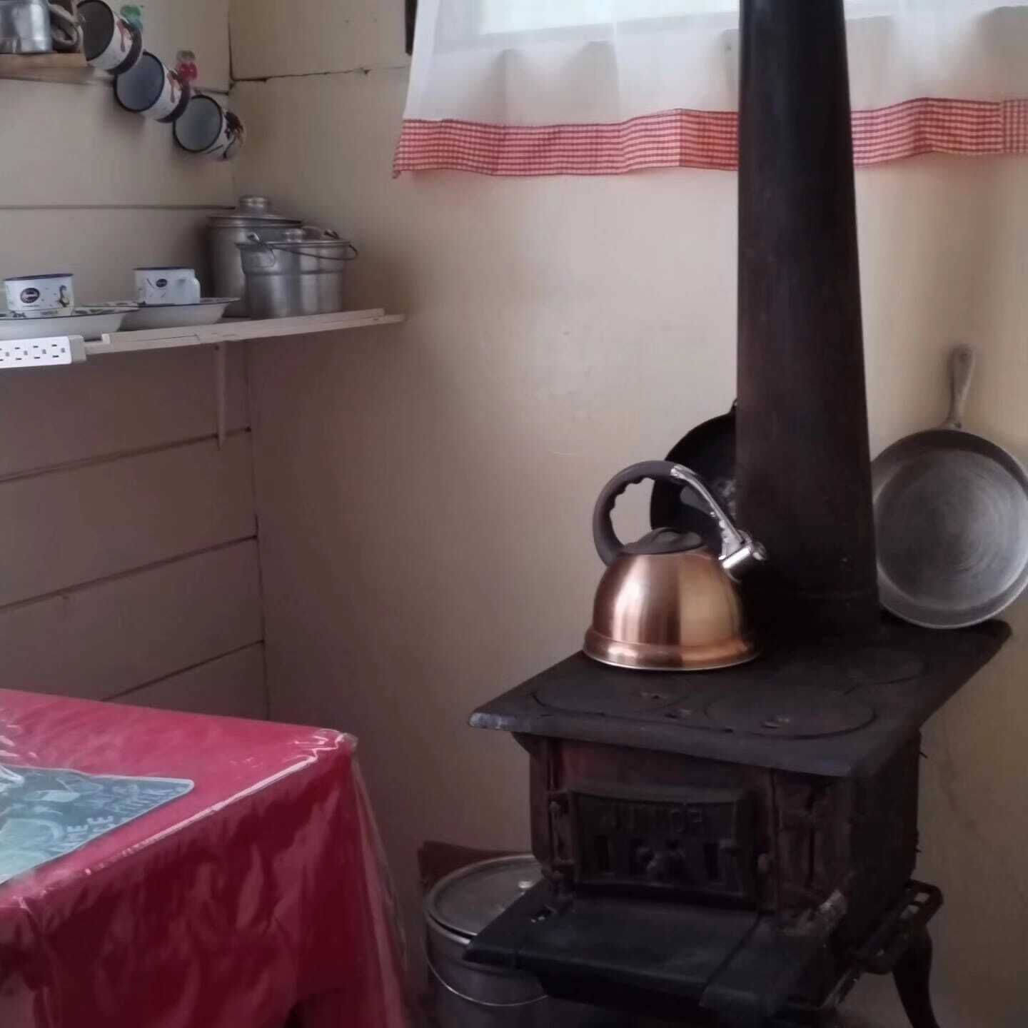 A kitchen with a stove, kettle, pots, and a red tablecloth.