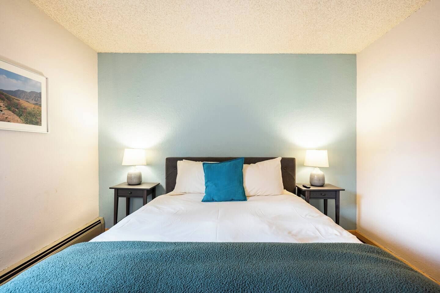 A hotel room with a bed, two bedside lamps, and a framed picture on the wall.