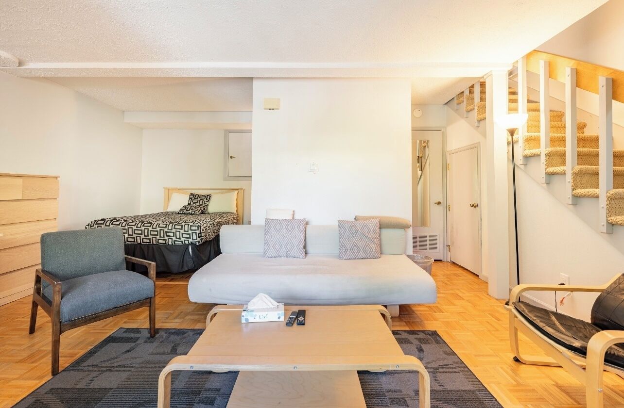 A hotel room with a bed, two armchairs, a coffee table, and a staircase with a patterned carpet.