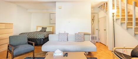 A hotel room with a bed, two armchairs, a coffee table, and a staircase with a patterned carpet.